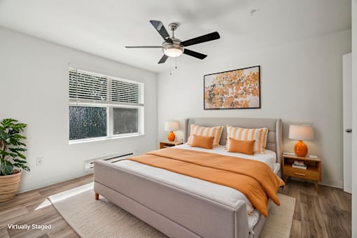 A bedroom with a bed, a ceiling fan, and a painting on the wall.