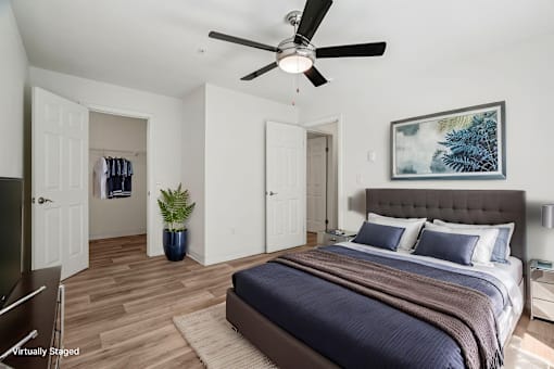 A bedroom with a bed, a ceiling fan, and a painting on the wall.