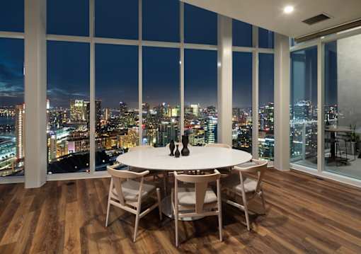 A dining table with chairs in front of a window overlooking a cityscape at night.