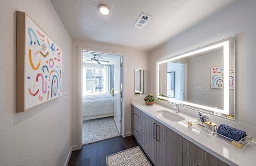 a bathroom with a sink and a mirror and a door to a bedroom