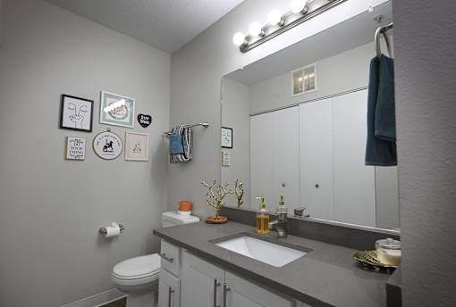 A bathroom with a toilet, sink, mirror, and wall decorations.
