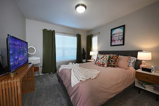 A bedroom with a bed, a television, and a window with blinds.
