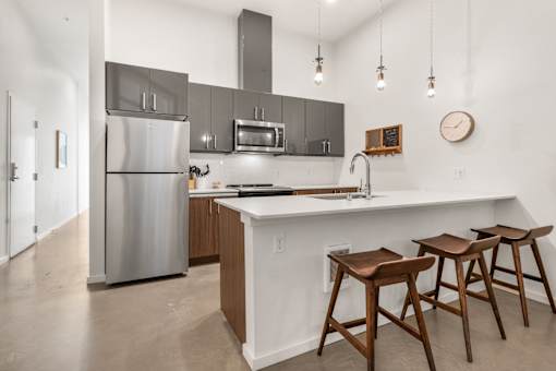 A kitchen with a refrigerator, oven, and bar stools.
