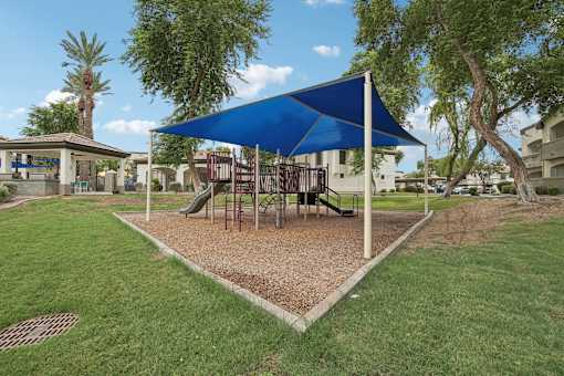 a playground with a swing set and a blue umbrella