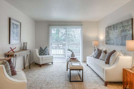 A living room with a white couch, a coffee table, and a window with a view of trees.