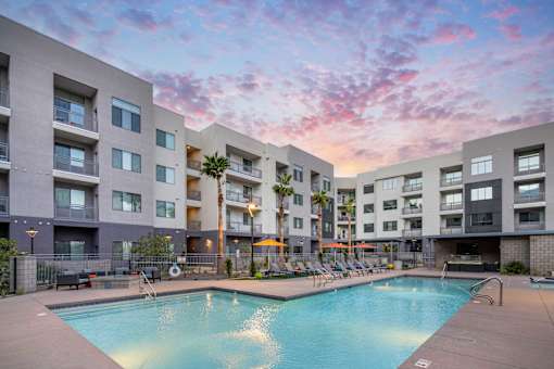 a swimming pool at an apartment complex with a sunset in the sky
