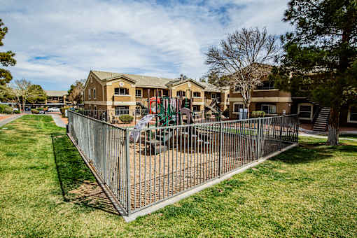 A playground area is enclosed by a fence in a grassy yard.