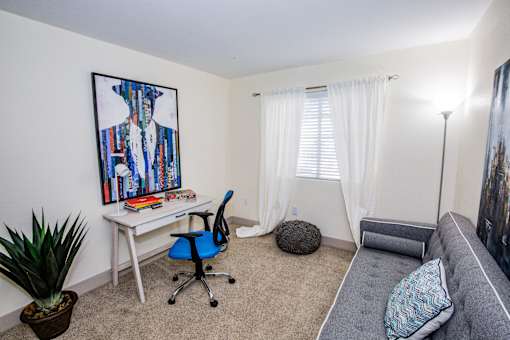 A room with a desk, chair, and a painting of a shirt on the wall.