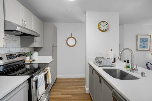 A kitchen with a stove, sink, and clock on the wall.