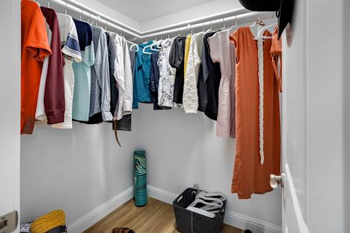 A white closet with clothes hanging and a black bag on the floor.
