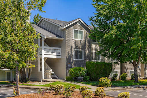 A grey house with a white balcony and a tree in front.