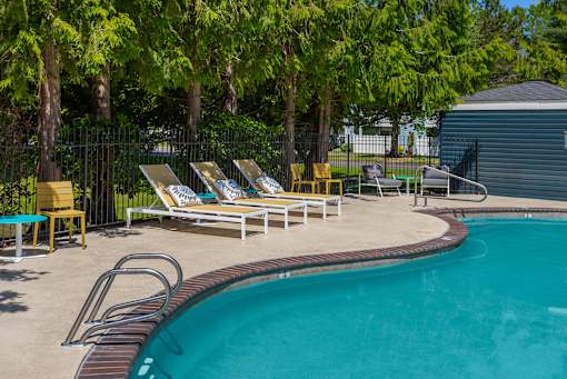 A pool surrounded by trees and chairs.