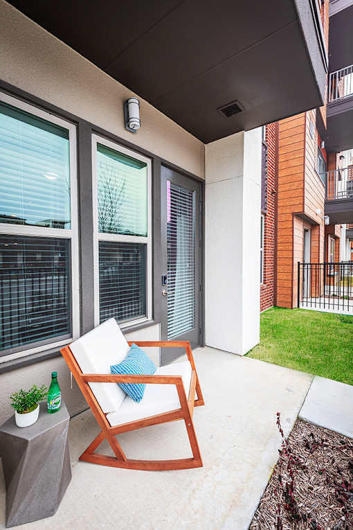 A patio with a chair and a table with a bottle on it.