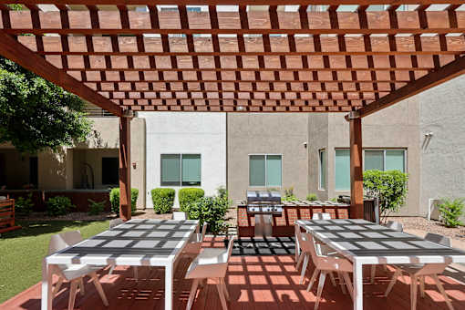 A patio with a table and chairs under a wooden pergola.