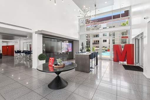 A large foyer with a black table in the middle and a red letter M on the wall.