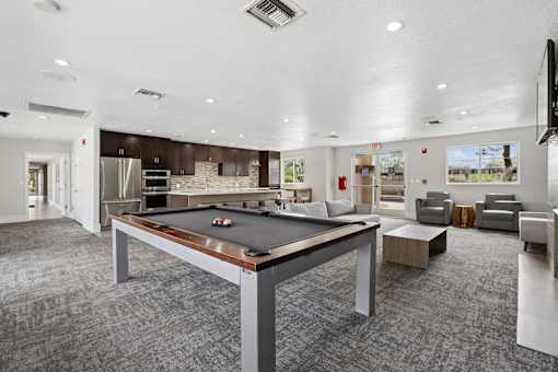 A billiard table is in the middle of a room with a television on the wall.