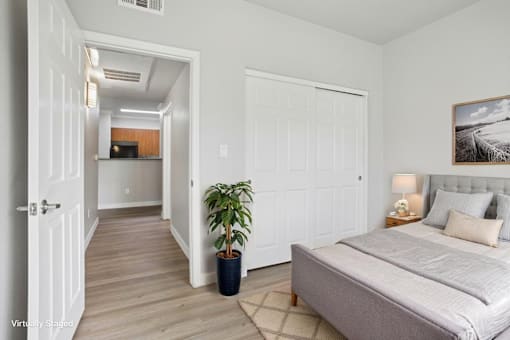 A bedroom with a bed, a potted plant, and a painting on the wall.