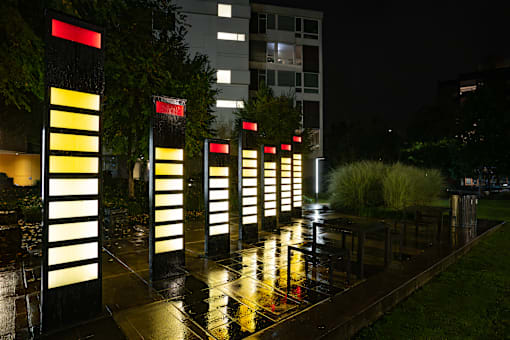 A series of lighted poles are lined up on a sidewalk.