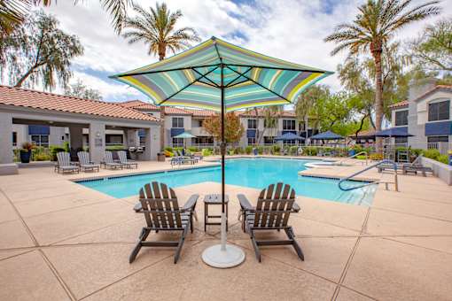 A pool with a striped umbrella and chairs.