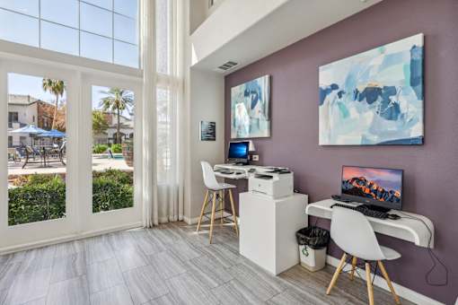 a room with a desk with a computer and chairs and a window