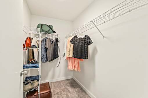 A white closet with clothes hanging and shoes on shelves.