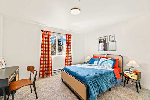 A bedroom with a bed, desk, chair, and window with curtains.