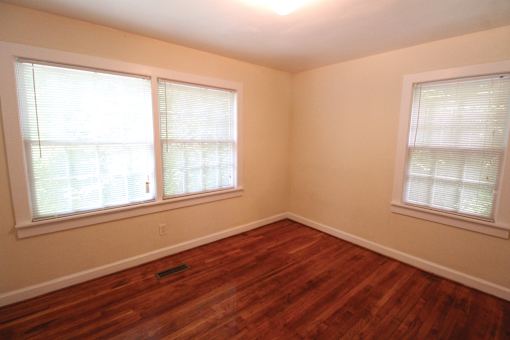 a bedroom with a hard wood floor and three windows