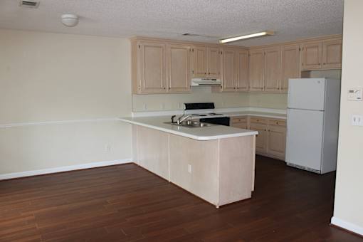 an empty kitchen with white appliances and wooden floors