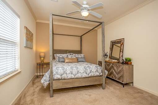 A bedroom with a four poster bed and a mirror on the dresser.