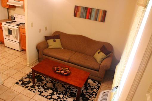 A brown couch with a pillow and a tray of food on a coffee table.