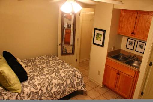 A bedroom with a bed and a small kitchen area.