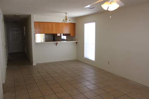 an empty living room with tile flooring and a kitchen