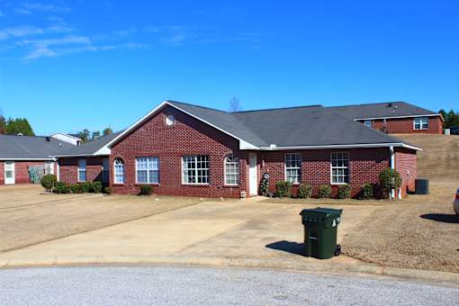 the front of a brick house with a driveway and a green trash can