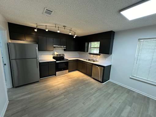 A kitchen with black cabinets and a stainless steel refrigerator.