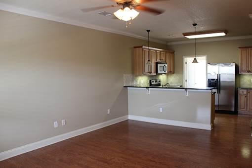 an empty living room with a kitchen and a ceiling fan