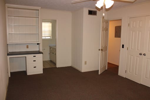 an empty living room with a kitchen with white cabinets