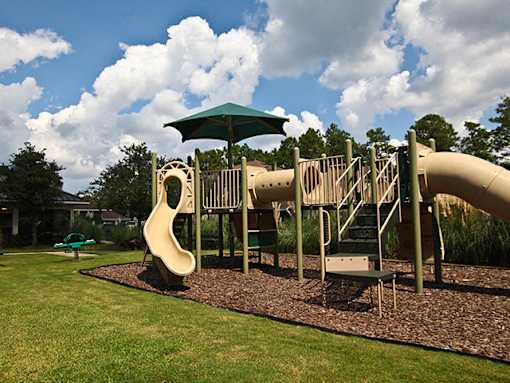 A playground with a green umbrella and a yellow slide.