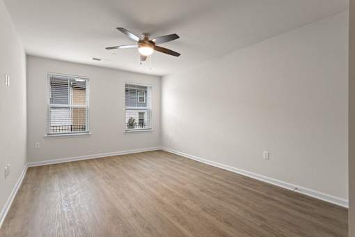 A room with a ceiling fan and two windows.