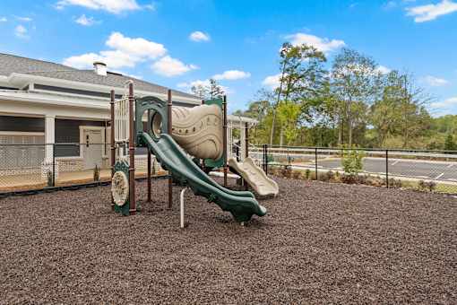 A playground with a green slide and brown ground.