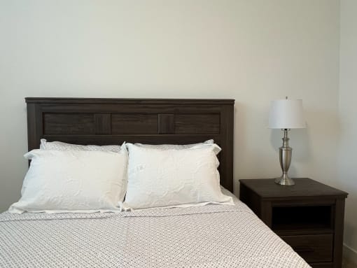 A bedroom with a bed and a nightstand with a lamp in The Alston Apartments.