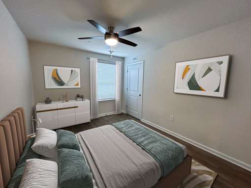 A bedroom with a bed, a ceiling fan, and two pieces of artwork on the wall.