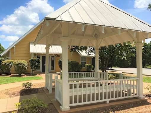A white gazebo is in front of a yellow house.