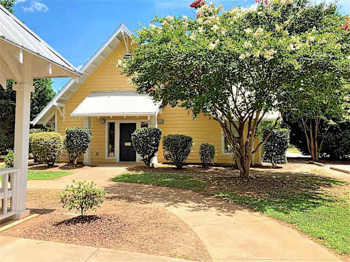 A yellow house with a white porch and a tree in front.