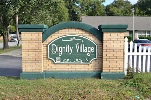 A sign that says Dignity Village is displayed on a brick wall.