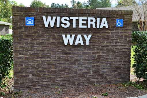 A sign that says Wisteria Way with a wheelchair and a house symbol.