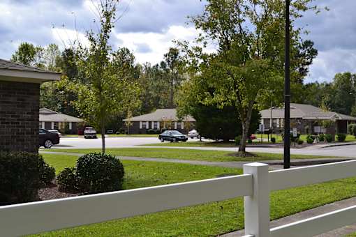 A white fence in front of a grassy area with houses and trees in the background.