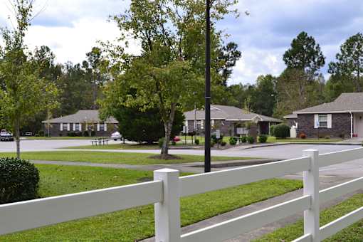 A white fence in front of a grassy area with houses in the background.