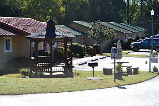 A gazebo is in the middle of a grassy area in front of a house.