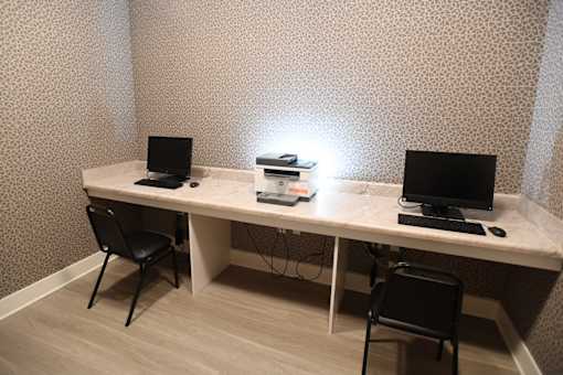 A white desk with two laptops and a stack of books under a lamp.