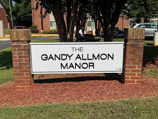 A sign that says "The Gandy Allmon Manor" is in front of a brick building.